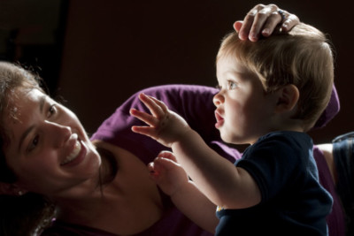 A mother rests her hand on a toddler's head, who is staring into a light