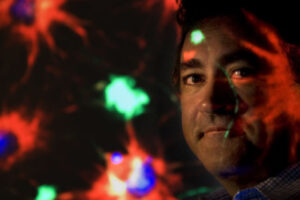 Charles Limoli stands in front of a bunch of colorful lights, some reflecting off his face