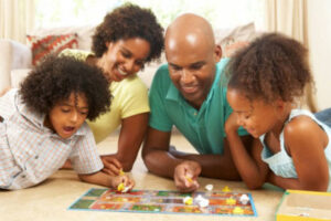 A family gathers around a board game on the floor