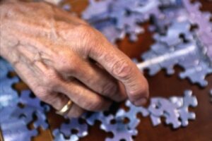 An elderly hand plays with puzzle pieces