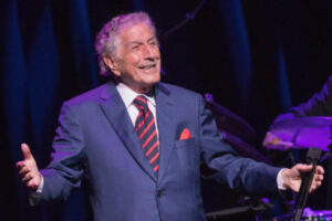 Image of Tony Bennett on stage, smiling and holding a microphone.