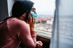 A masked female is looking through a window.