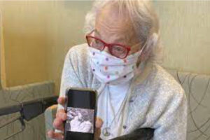Image of Carol Robertson, a masked female senior, holding a smart phone with a of herself at a younger age.