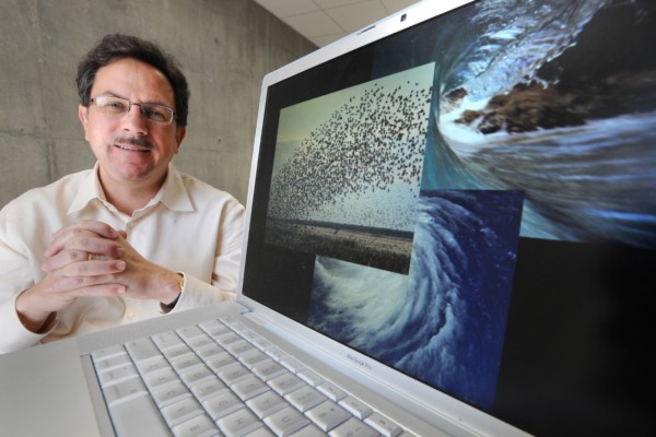 Male researcher poses next to a laptop displaying images of nature.