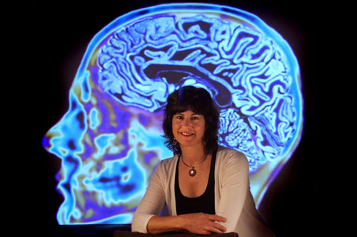 Image of Leslie M. Thompson Ph.D. posing in front of an MRI image.