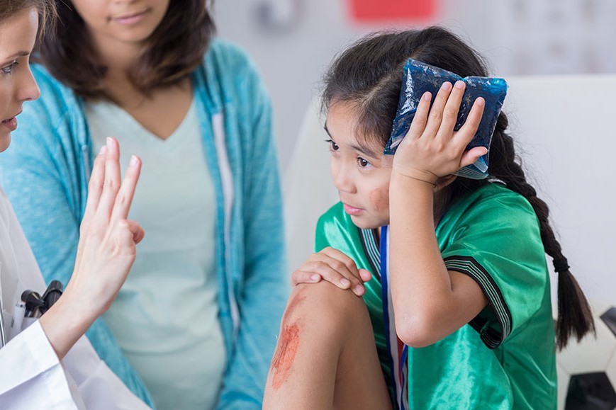 A girl with a scraped knee holds an ice pack to her head and is looking at a doctor holding up 3 fingers