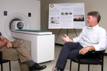 Greg Hickock sits in front of a mri scanner, talking to someone off screen.