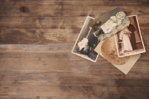 4 old greyscale photos consisting of baby pics, a wedding, and a child lay on an aged wooden backdrop.