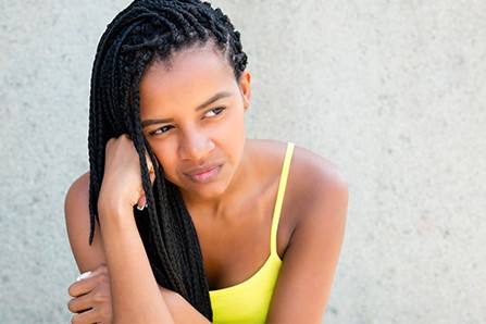 A young black woman rests her head on her arm, looking off into the distance with a disgruntled expression.