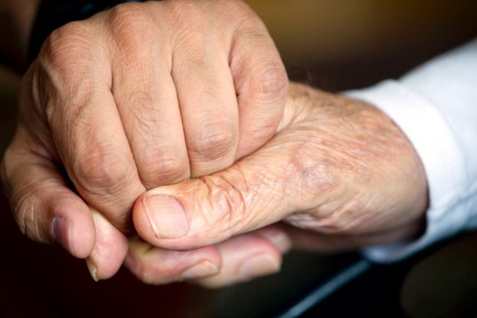 Two wrinkled hands clutch each other in an affectionate gesture