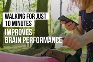 A woman is on her phone in the forest holding some kind of bag. Text reads "Walking for just 10 Minutes improves brain performance