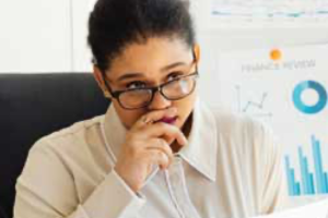 A woman with glasses peers over her lenses, hand hovering over her mouth in a thinking position. To the right is some data charts highlighted in blue.