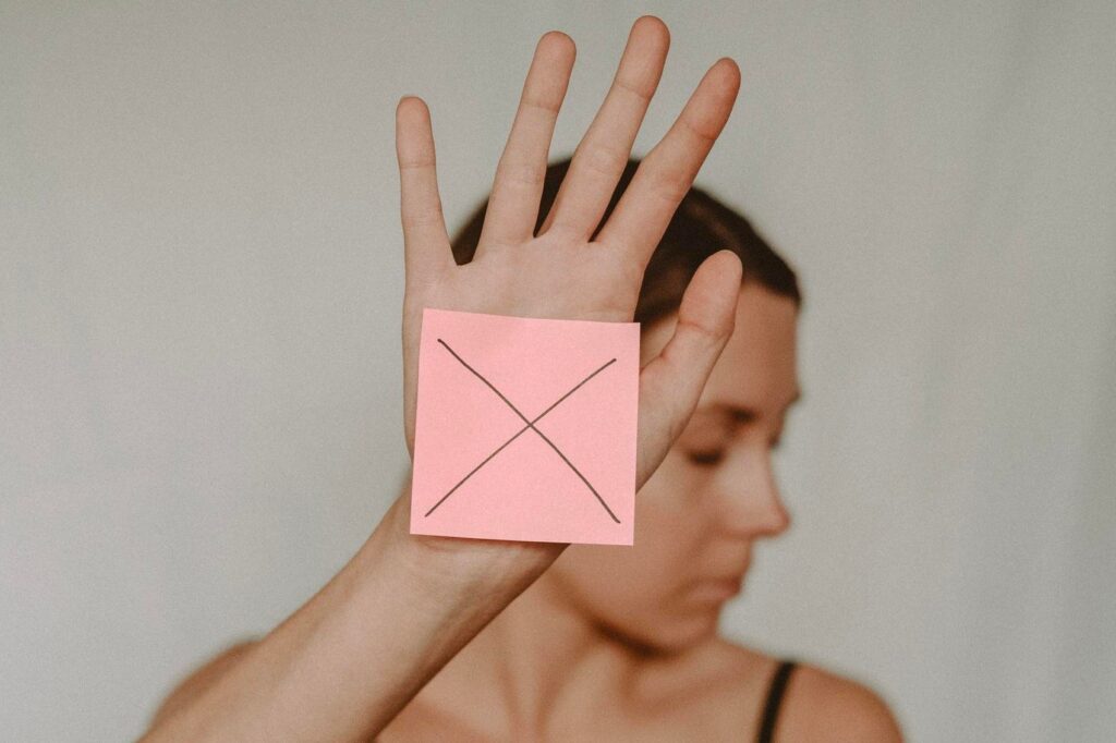 A woman holds a sticky note with an X on it toward the camera and looks away.