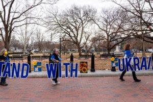 3 People march on the street holding words that read "Stand With Ukraine"