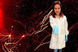 Scientist displays something in hand in front of neuron image.